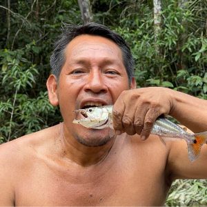 Hombre sosteniendo una piraña en la selva amazónica, mostrando las tradiciones de pesca local en Iquitos, Perú.