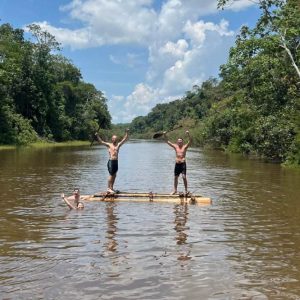 Turistas disfrutando de una balsa artesanal en un río de la Amazonía peruana, rodeados de exuberante selva tropical bajo un cielo despejado.