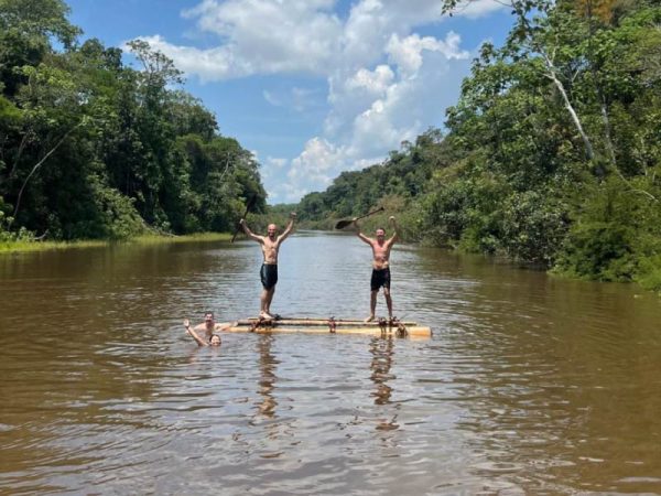 Turistas disfrutando de una balsa artesanal en un río de la Amazonía peruana, rodeados de exuberante selva tropical bajo un cielo despejado.