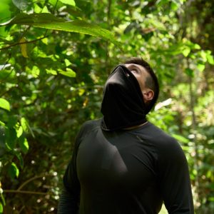 Explorador amazónico observa el dosel del bosque en medio de una selva verde y densa, con rostro parcialmente cubierto.