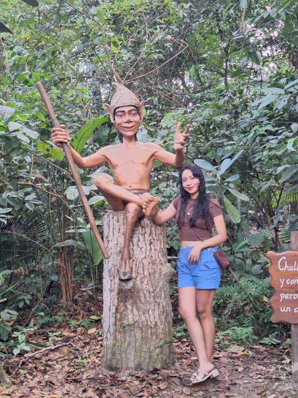 Turista junto a escultura del Chullachaqui, personaje mítico de la Amazonía peruana, en medio de la selva.