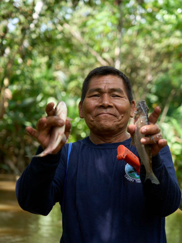 Persona mostrando dos peces capturados en la Amazonía peruana, rodeado de vegetación selvática y vestido con ropa de campo.