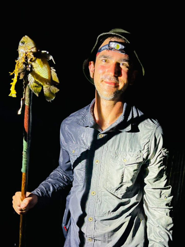 Persona sostiene un pez amarillo capturado durante una jornada de pesca nocturna en la selva amazónica.
