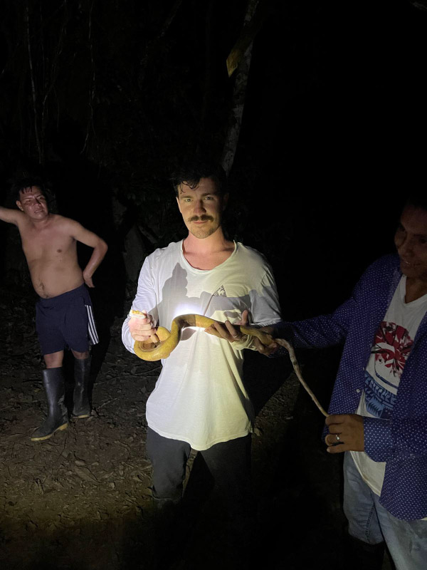 Tres personas interactúan con una serpiente durante una actividad nocturna en la Reserva Nacional Pacaya Samiria, rodeados de vegetación selvática.