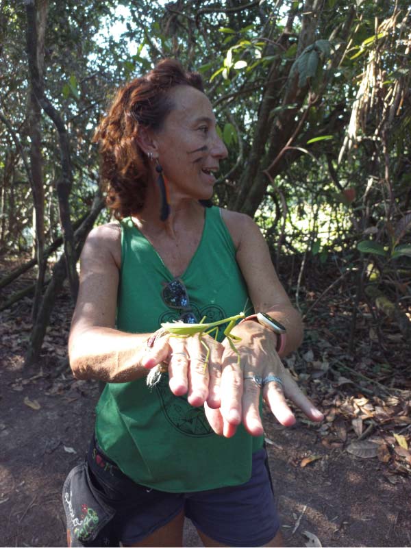 Turista sonriente, con pintura facial indígena, sosteniendo un Insecto Palo grande y verde en sus manos, durante un tour de entomología y trekking en la selva amazónica.