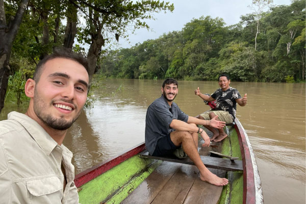 Mejores Tours en la Selva de Iquitos Una Aventura Auténtica Dos turistas jóvenes y un guía local navegando alegremente por un afluente del río Amazonas en una canoa tradicional de madera durante un tour de exploración