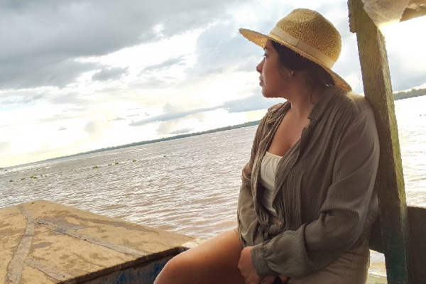¿Cuándo viajar a Iquitos Clima, Temporadas y Consejos de Viaje Una viajera con sombrero de paja contempla la inmensidad del río Amazonas desde una embarcación bajo un cielo nublado durante la vacante del río.