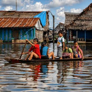 Children paddling a small wooden canoe through the flooded streets of Belén Market in Iquitos, surrounded by traditional Amazonian stilt houses.